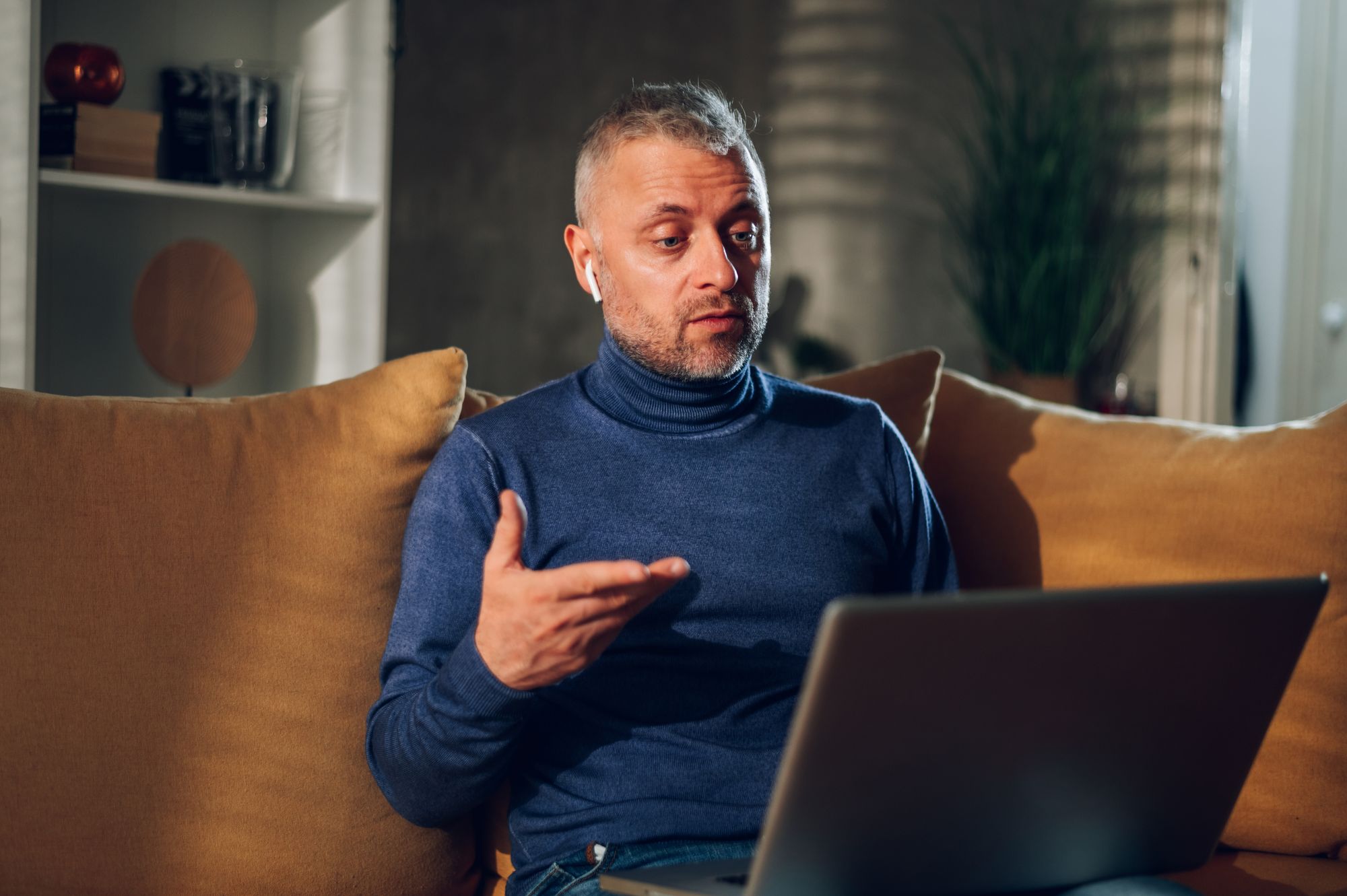 Mann im Wohnzimmer im Videogespräch am Laptop